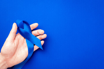 Men cancer. Blue ribbon in hands isolated on deep blue background. Awareness prostate cancer of men health in November. Adrenocortical carcinoma concept.