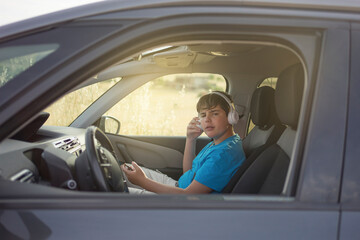 boy sitting in a car, listening to music on his cell phone looking at the camera