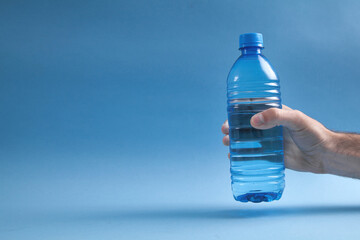 Male hand holding bottle of water on blue background.