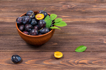 Fresh ripe plum fruits whole and chopped with leaves in a bowl on a wooden brown table. Summer harvest.