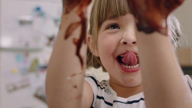 happy little girl with hands covered in chocolate licking fingers having fun baking in kitchen naughty child playing enjoying childhood