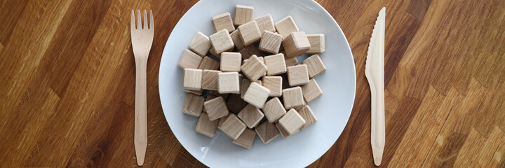 Wooden cubes lying on plate near knife and fork closeup