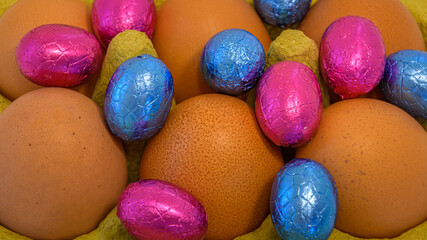 Fototapeta na wymiar chocolate eggs in folio between uncooked eggs. Easter concept background