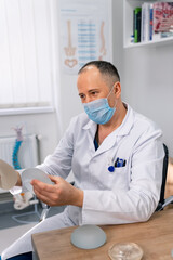 Doctor in mask showing silicon medical implants. Surgeon in medicine uniform holding new implants in hands. Stock photo