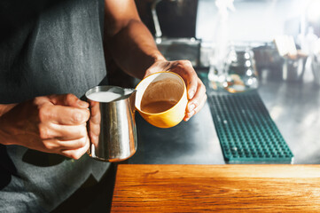 Fototapeta na wymiar brown adult latin man, holding a yellow cup and a steel carafe preparing a latte in a coffee shop