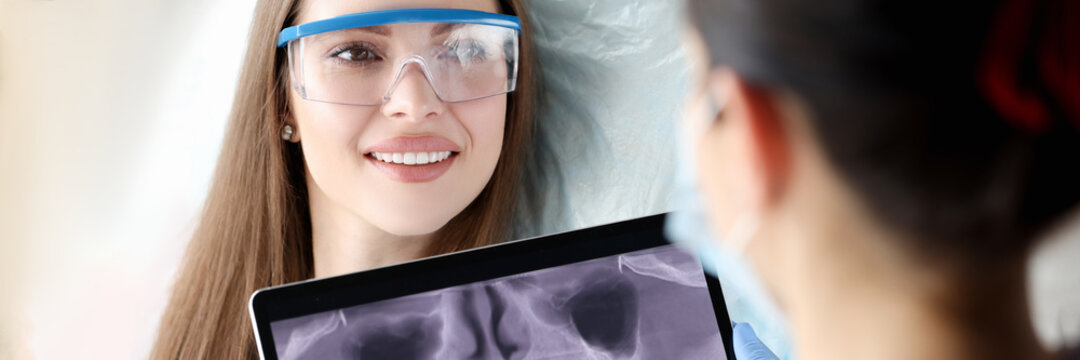 Dentist holding digital tablet with 3D picture of teeth in hands in front of female patient