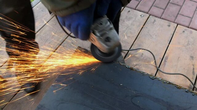 The process of electric grinding of steel structures. Bright flames and sparks. Master in work gloves.