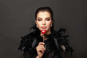 Valentine's Day. Attractive woman brunette holding red heart near her lips on black portrait