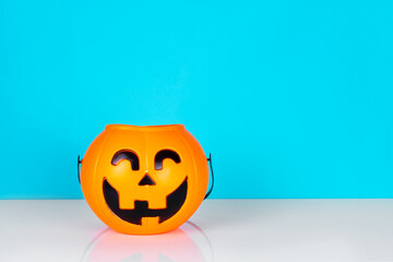 Orange plastic basket halloween pumpkin on white table and blue background