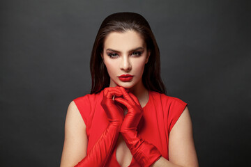 Stylish woman brunette with makeup and dark hair wearing red dress and red silk gloves on black...