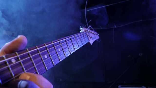 Guitarist playing electric guitar in bright flickering light on stage. Hand, guitar fingerboard and strings close-up.