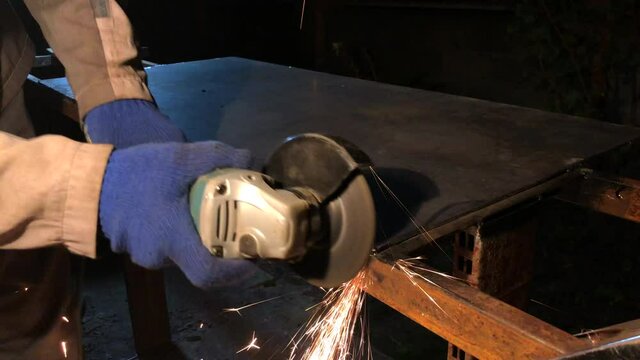 The process of electric grinding of metal structures. Bright flames and sparks. Master in work gloves.
