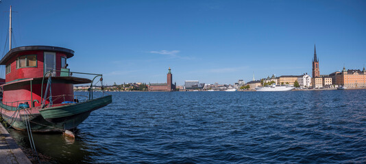 Obraz premium Boats at the bay Riddarfjärden and the island Kungsholmen with the Town City Hall and the pier Norr Mälarstrand a sunny day, seen from the pier Söder Mälarstrand