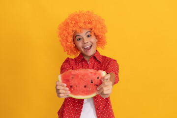 amazed kid in fancy orange hair wig holding fresh ripe water melon slice fruit, organic food
