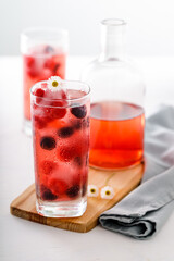 Two tall glasses with red fruit juice on ice and bottle in the foreground with small flowers