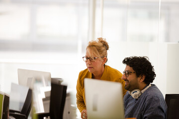 Business people talking at computer in open plan office © KOTO