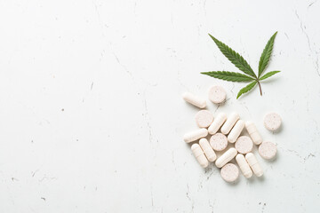 CBD pills and green leaf at white table. Alternative medicine. Sedative, antibiotic, antioxidant using cannabis products.