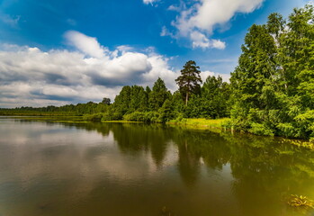 Fototapeta na wymiar River banks against blue sky with white clouds in summer