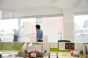 Businessman and businesswoman discussing diagram sketches hanging on conference room window