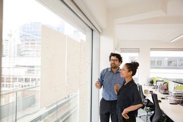 Business people discussing diagram sketches hanging on office window