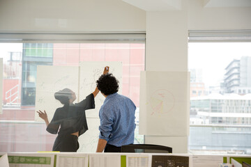 Businessman and businesswoman discussing diagram sketches hanging on conference room window
