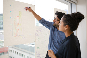 Business people discussing diagram sketches hanging on office window