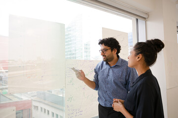Business people discussing diagram sketches hanging on office window