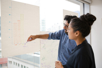 Business people discussing diagram sketches hanging on office window