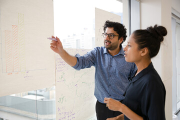 Business people discussing diagram sketches hanging on office window