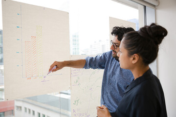 Business people discussing diagram sketches hanging on office window