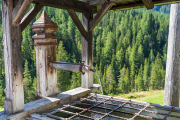 Vintage wooden faucet with drinking water on a wooded mountain road in the Dolomites, Italy