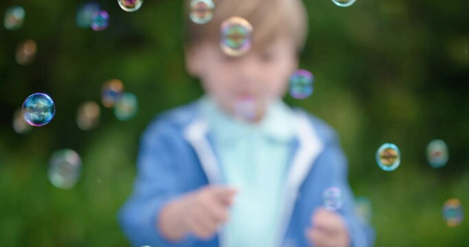 happy little boy playfully catching soap bubbles floating with cute child having fun popping bubbles in sunny park carefree childhood game 4k