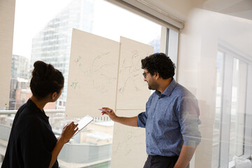 Businessman and businesswoman discussing diagram sketches hanging on conference room window