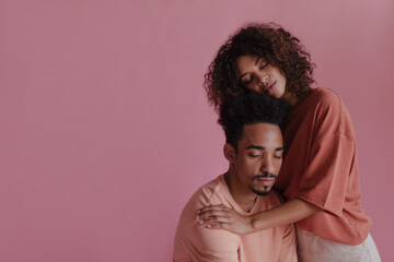 Fototapeta na wymiar Peaceful studio portrait of two African lovers with closed eyes against pink background. Woman hugs her husband tenderly and full of love on pink background. Positive emotions, concept.