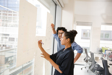 Business people discussing diagram sketches hanging on office window