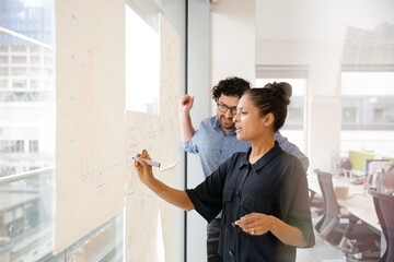 Business people discussing diagram sketches hanging on office window