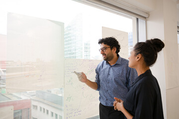 Business people discussing diagram sketches hanging on office window