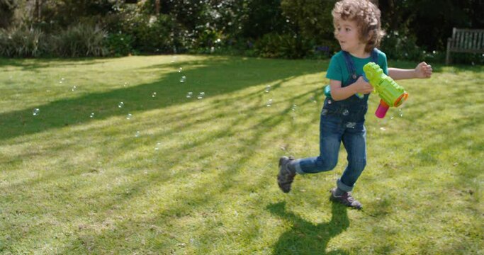 happy little boy blowing soap bubbles playing in sunny garden running with toy gun enjoying fun game funny playful child enjoying summer 4k