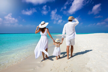 A elegant family in white summer clothing walks hand in hand down a tropical paradise beach and...