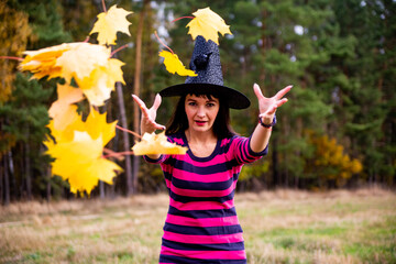 witch throws leaves in the autumn forest. Halloween costume party magician