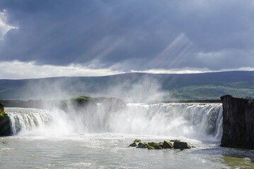 Godafoss waterfall in Iceland, a gloomy cloud in the sky, contrasting sun rays