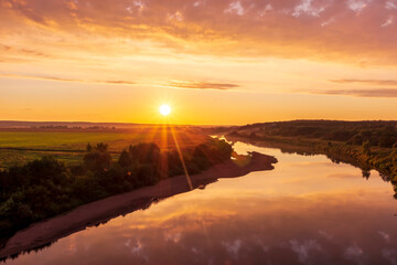 Scenic view at beautiful summer river sunset with reflection on water with green bushes, calm water ,deep colorful cloudy sky and glow on horizon on a background, spring evening landscape