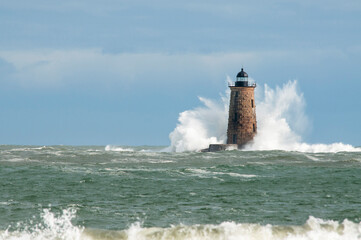 Giant Waves Surround Stone Lighthouse in Maine As Sun Breaks Through Clouds