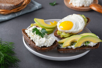 Sandwiches with a minced curd, avocado, fried eggs and herbs on the natural wooden cutting board. Healthy food concept