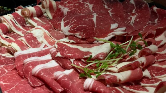 Chinese spicy hotpot soup. Plate with raw meat slides of beef at the table in a restaurant. Typical hot pot herbal cuisine with fresh and delicious dishes in chafing dish at Taiwan-Dan