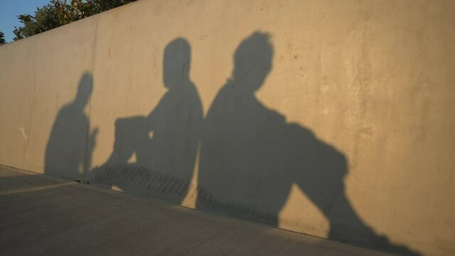 Shadows of argued couple sitting back to back as male silhouette passing and woman leaving man. Unrecognizable boyfriend and girlfriend breaking up in sunlight outdoors. Slow motion