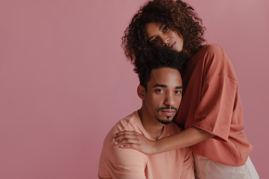 Brazilian family portrait of young brother and sister in pink photo studio. Image lovely curly-haired sublime brown skinned people wearing peach T-shirt. Home comfort concept