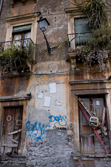 Fototapeta na wymiar Fasada starego budynku w Katanii, na Sycylii. Zaniedbane balkony z kwiatami.