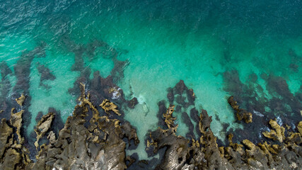 Bird's eye view of clear blue waters with coral reefs and rocks on a tropical island.