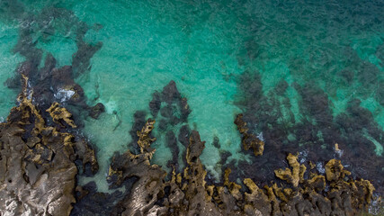 Bird's eye view of clear blue waters with coral reefs and rocks on a tropical island.
